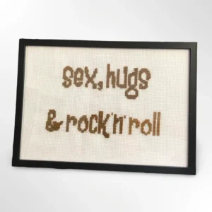 Håndlaget korssting-broderi med teksten "sex, hugs & rock'n'roll" innrammet i svart ramme, 21 x 30 cm. Laget av Fiffis gaver.