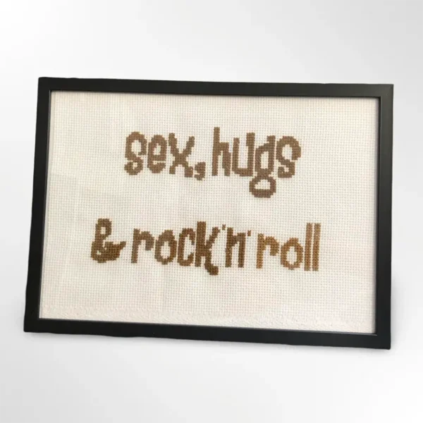 Håndlaget korssting-broderi med teksten "sex, hugs & rock'n'roll" innrammet i svart ramme, 21 x 30 cm. Laget av Fiffis gaver.