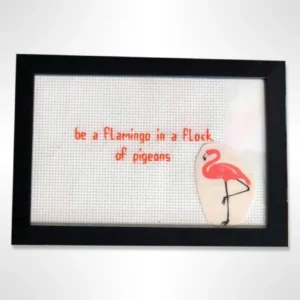 Unikt broderi med teksten 'Be a Flamingo in a Flock of Pigeons'. Inkludert i svart ramme, perfekt for hjemmet eller som gave.