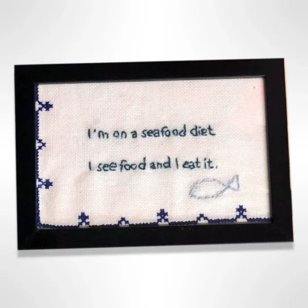 Håndlaget broderi med morsom tekst: "I'm on a seafood diet: I see food and I eat it". Kompakt størrelse (10x15 cm) og perfekt som gave eller veggpynt.