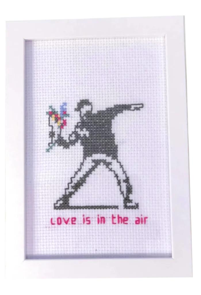 Håndlaget broderi inspirert av Banksys kunstverk "Love is in the Air". En unik dekorasjon for kunstelskere. Dimensjoner: 10 x 15 cm.